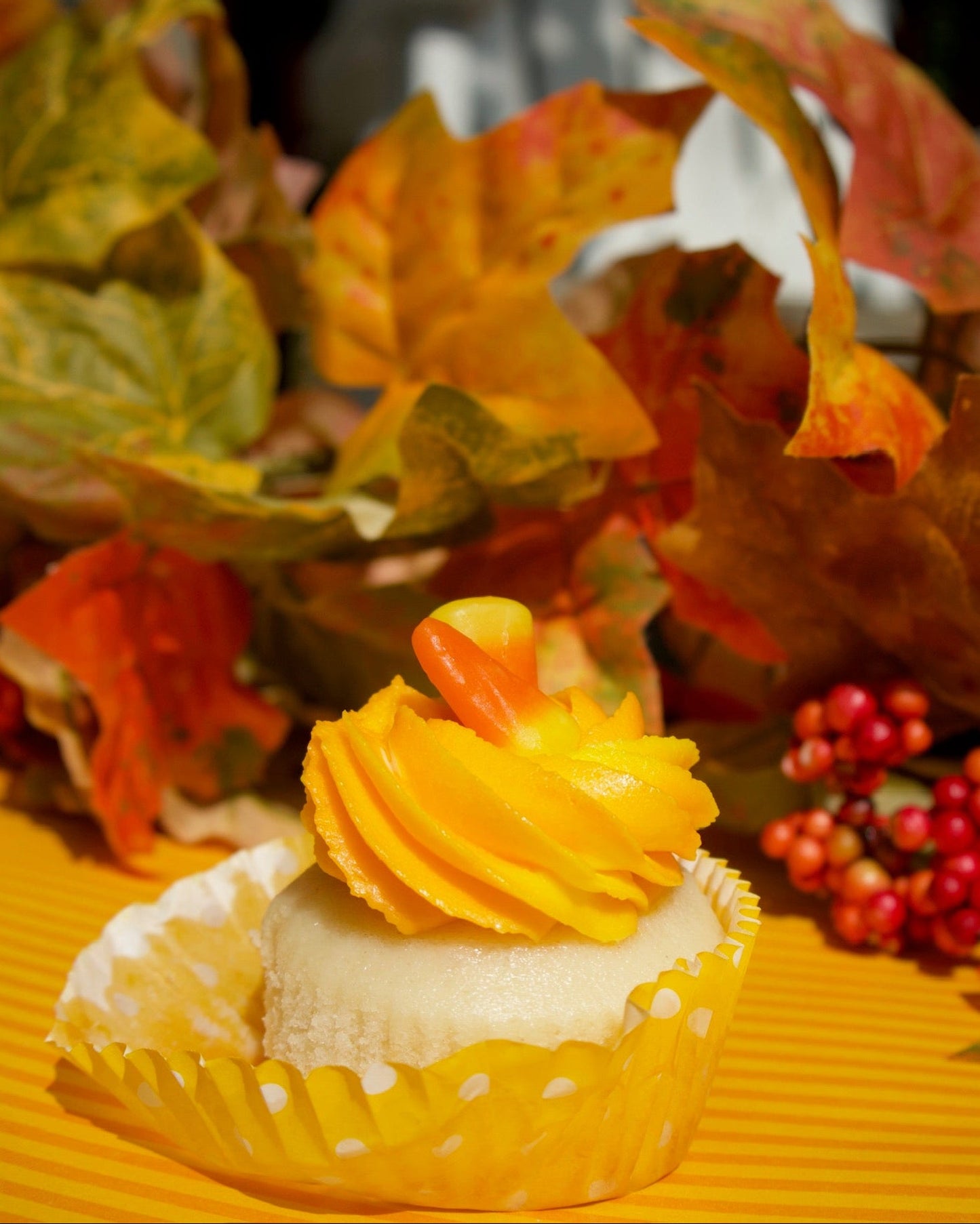 Cupcake with yellow frosting and candy corn on a yellow surface with autumn leaves and berries.