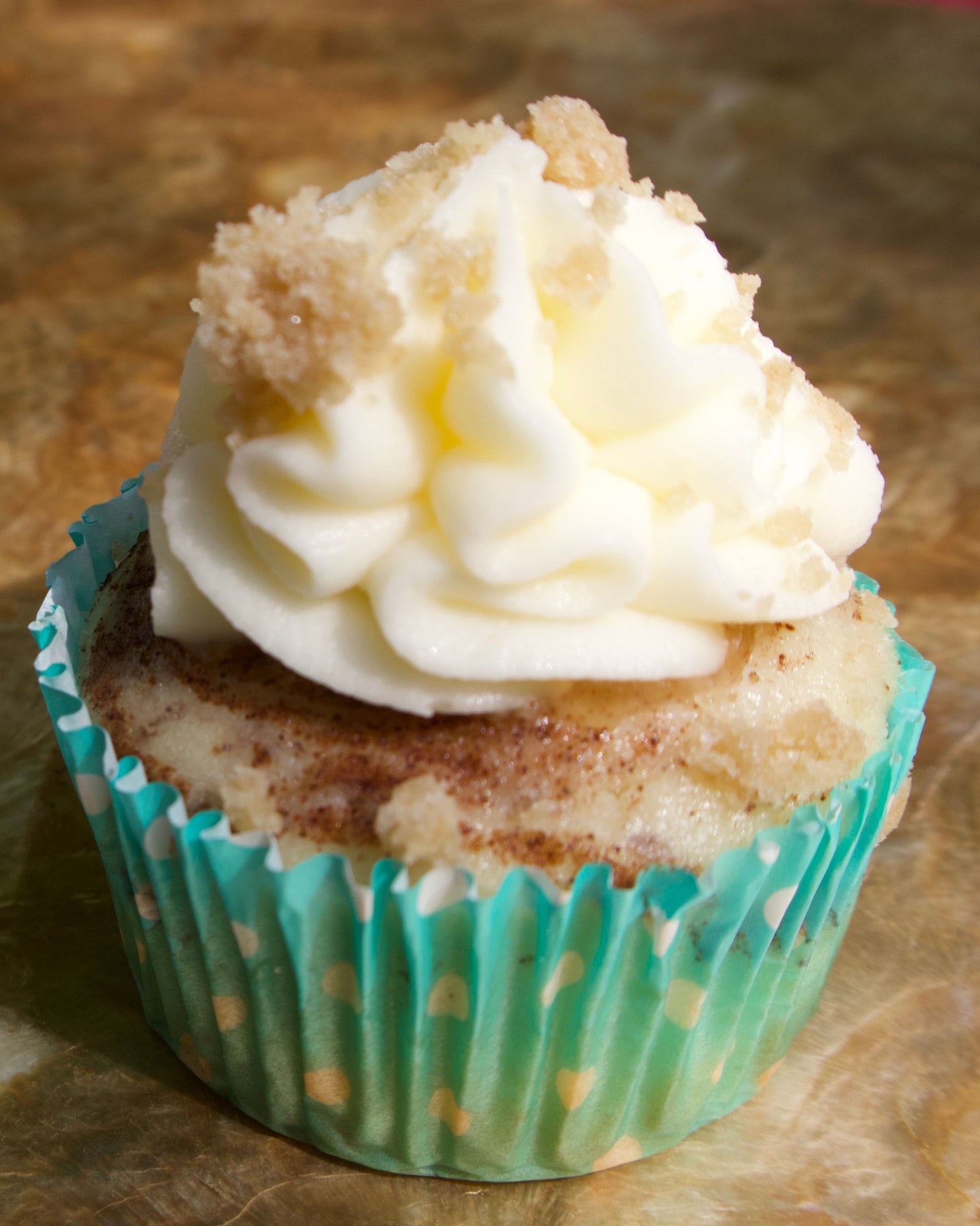 Cupcake with white frosting and a crumbly topping on a metallic surface