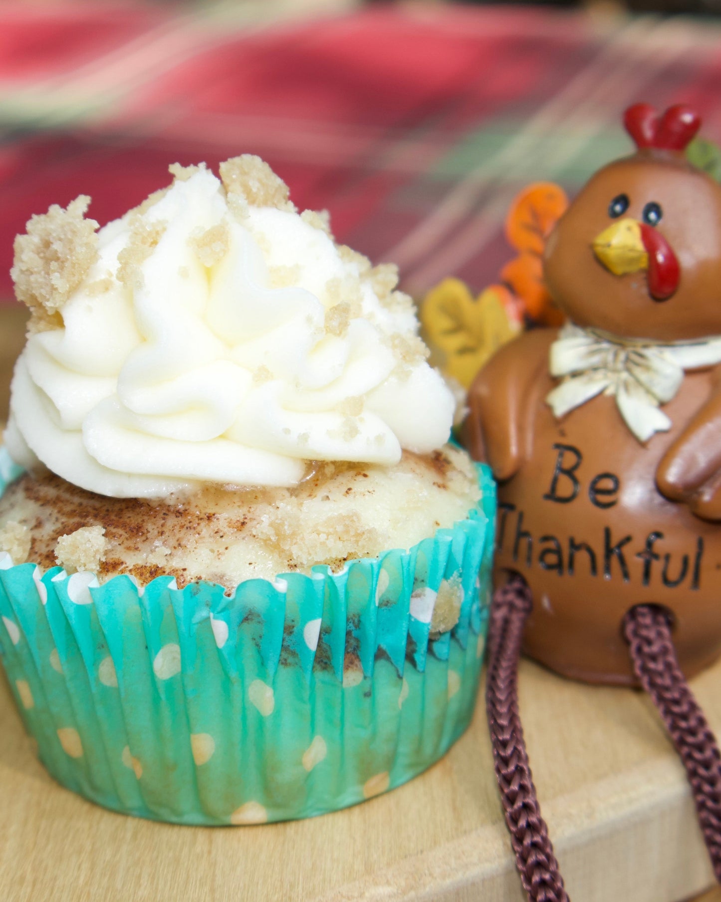 Cupcake with white frosting and a small decorative turkey figurine on a wooden surface.