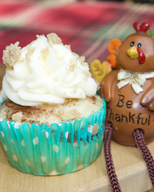 Cupcake with white frosting and a small decorative turkey figurine on a wooden surface.